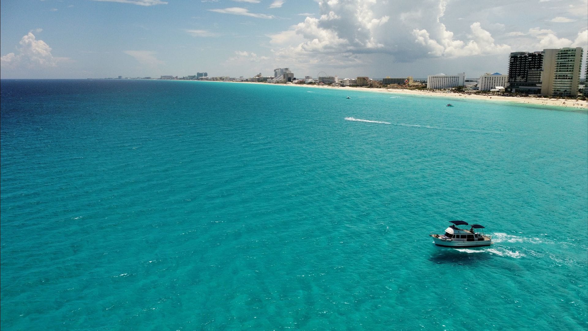 Aerial view of the Tafil cruising the turquoise bay with the Cancún Hotel Zone coastline behind