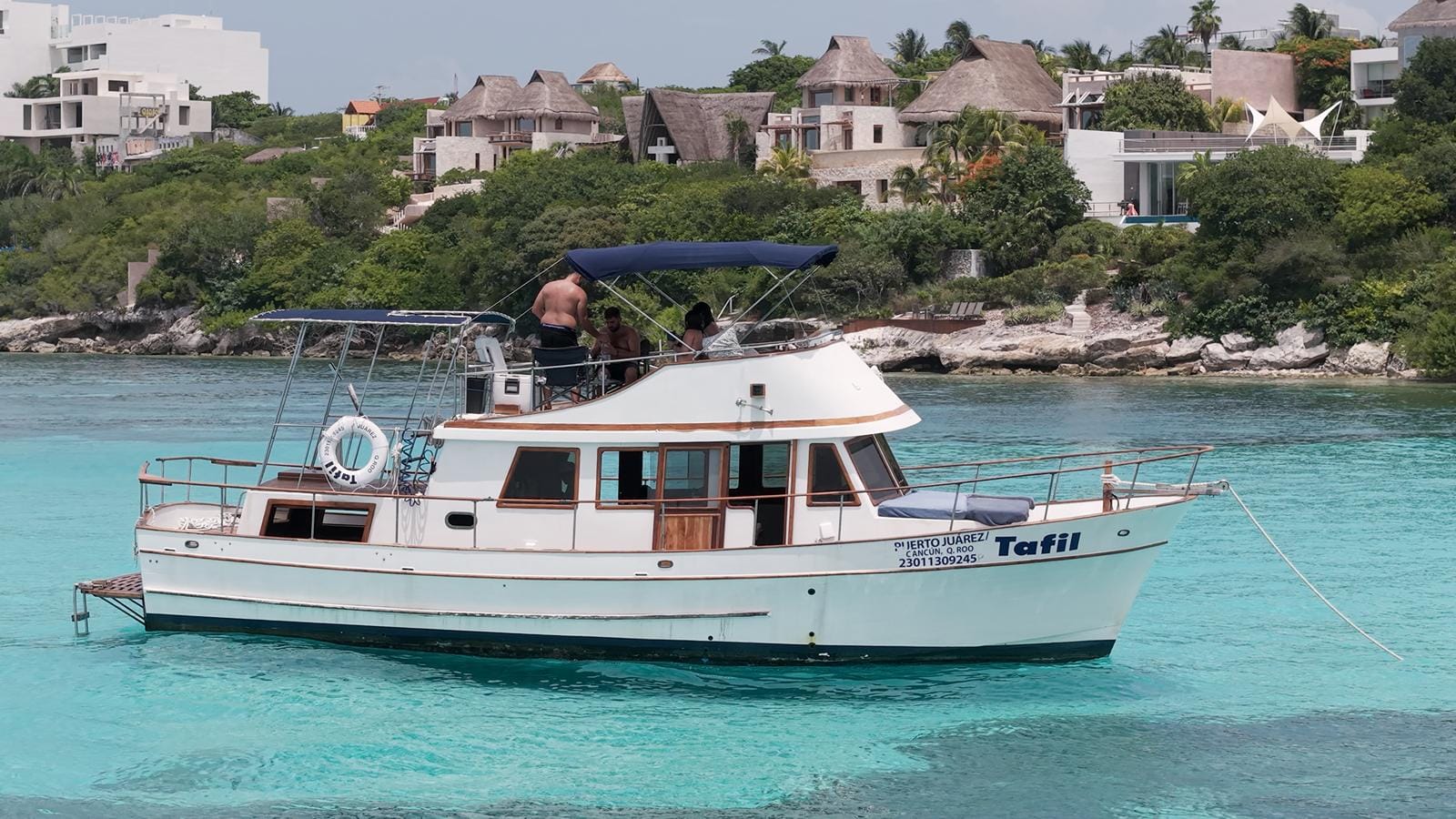 The Tafil cruising along the Isla Mujeres coastline with houses and palms behind