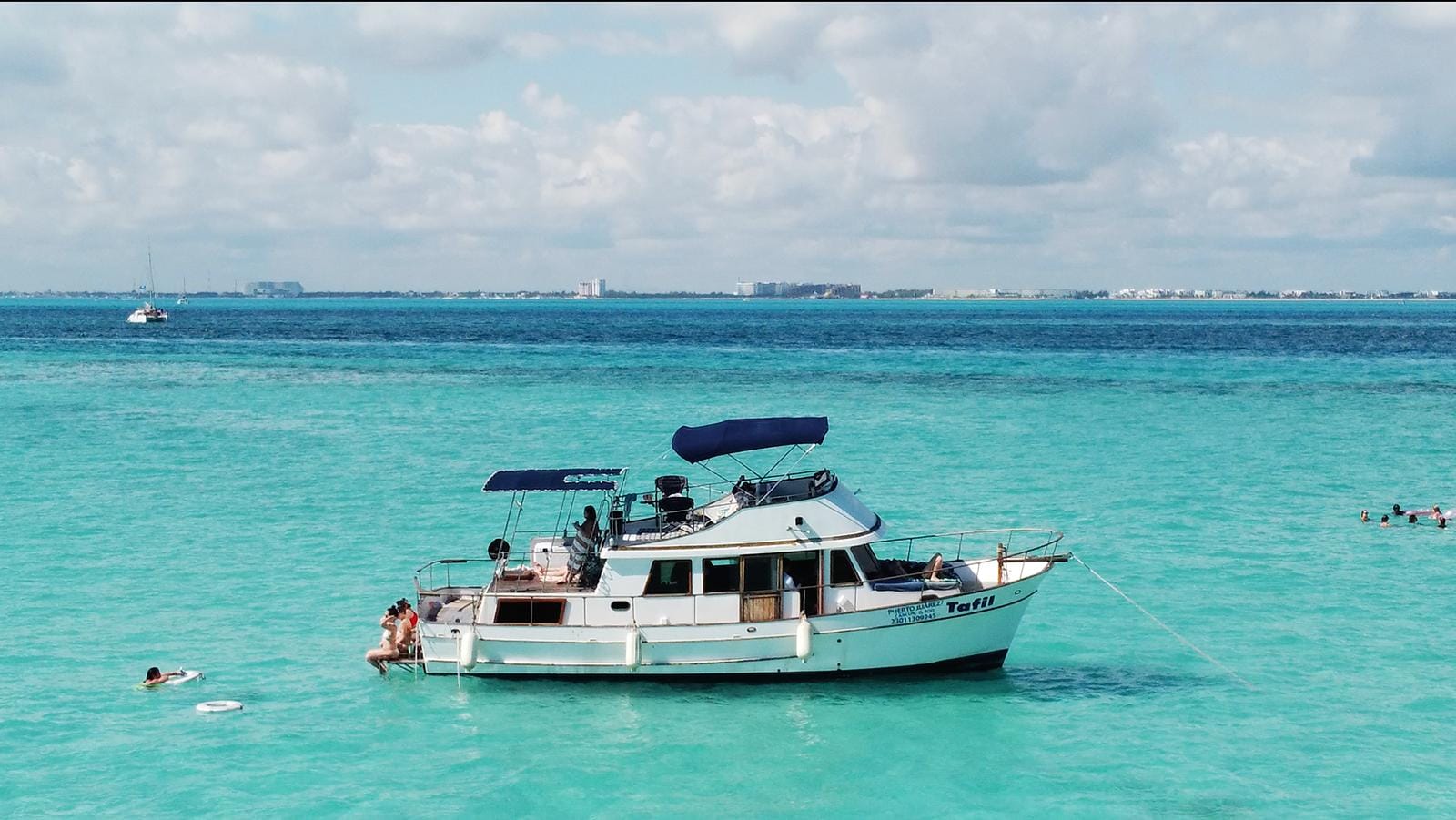 The Tafil anchored in calm turquoise water off Isla Mujeres with the Cancún skyline on the horizon